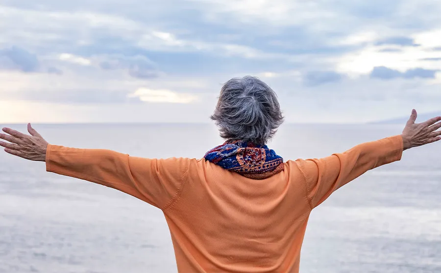 Femme âgée de dos face à la mer, évoquant l’autonomie des seniors